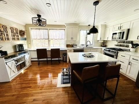 kitchen featuring a kitchen island, decorative light fixtures, light countertops, appliances with stainless steel finishes, and dark wood-style floors