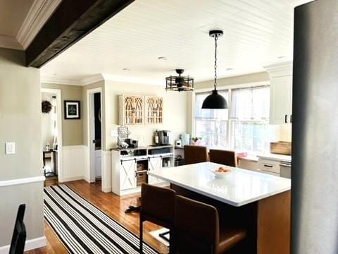 kitchen featuring ornamental molding, decorative light fixtures, wood finished floors, white cabinets, and light countertops