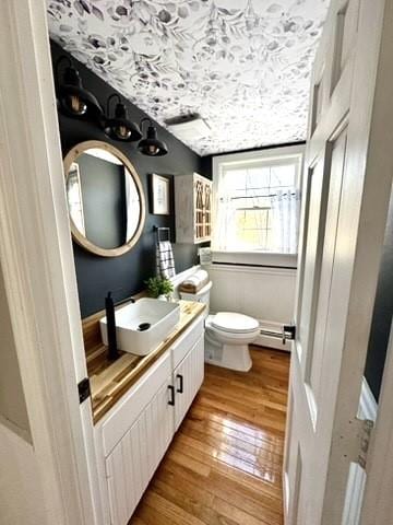 half bathroom featuring vanity, toilet, wood-type flooring, and a baseboard radiator