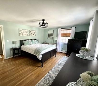 bedroom with a baseboard heating unit, baseboards, and wood finished floors