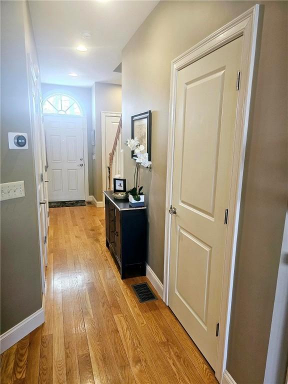 doorway with visible vents, baseboards, light wood-style flooring, and stairs