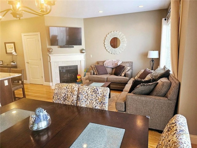 living room featuring light wood-style flooring, a tiled fireplace, recessed lighting, an inviting chandelier, and baseboards