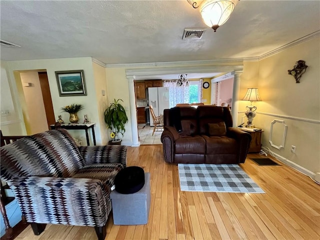 living area with decorative columns, light wood-style floors, visible vents, and crown molding