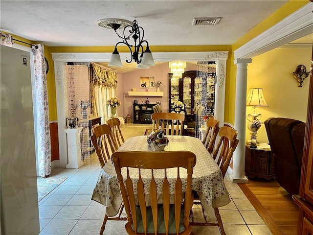 dining space with light tile patterned floors, visible vents, an inviting chandelier, and decorative columns