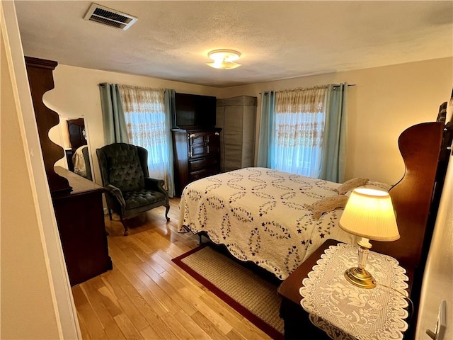 bedroom with visible vents, a textured ceiling, and light wood finished floors