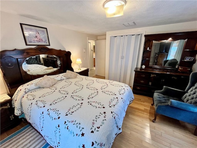 bedroom featuring a closet, visible vents, a textured ceiling, and wood-type flooring