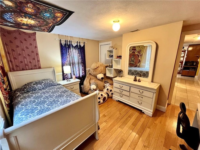 bedroom with visible vents, light wood-style floors, and a textured ceiling