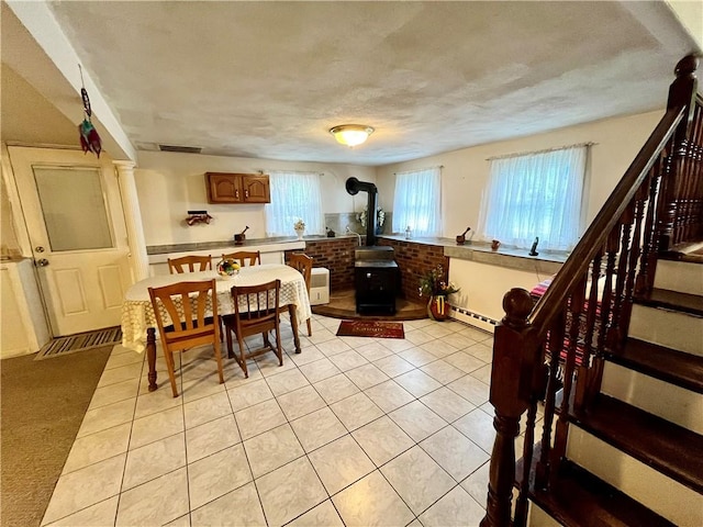 dining space featuring visible vents, stairs, light tile patterned floors, a wood stove, and a baseboard radiator