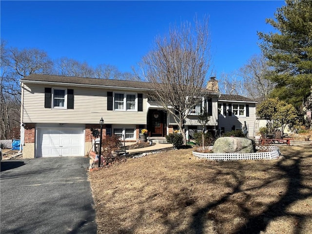 bi-level home featuring aphalt driveway, a chimney, a garage, and brick siding