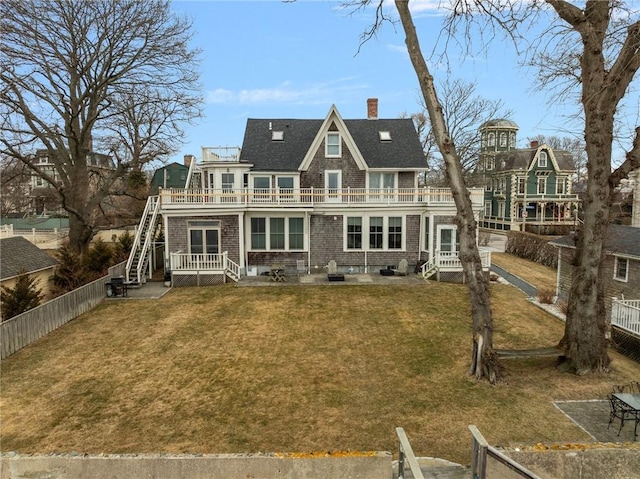 rear view of house featuring a balcony, a chimney, a lawn, and fence