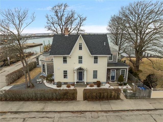 view of front of property with a shingled roof, fence, a water view, and a chimney