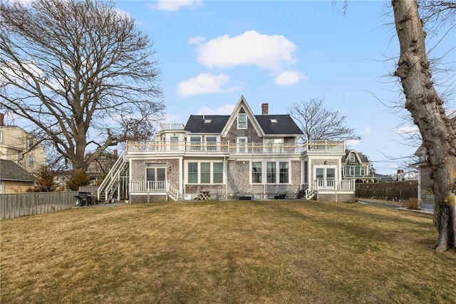 back of house featuring a balcony, a lawn, a chimney, and fence