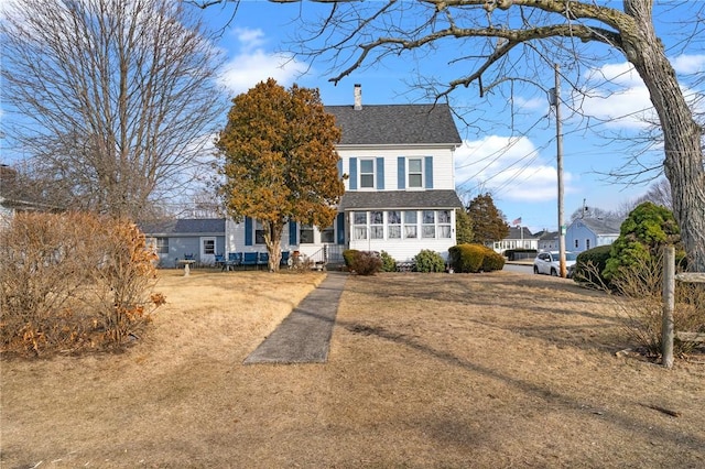 traditional-style home featuring a shingled roof, a front yard, and a chimney