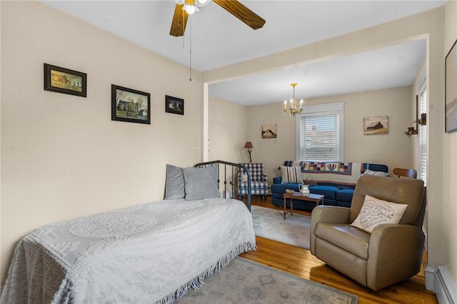 bedroom with baseboard heating, ceiling fan with notable chandelier, and wood finished floors