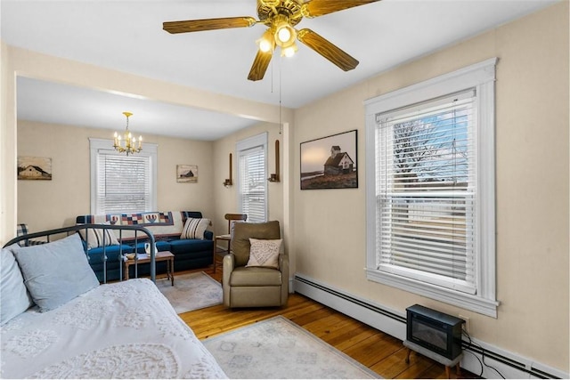 living room featuring ceiling fan with notable chandelier, a baseboard heating unit, and wood finished floors