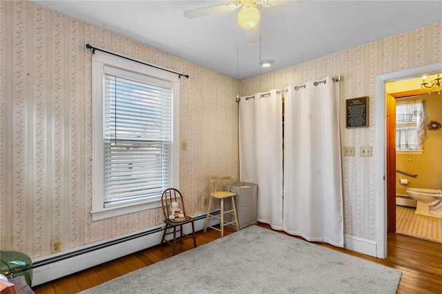 interior space with wallpapered walls, ceiling fan, wood finished floors, and a baseboard radiator