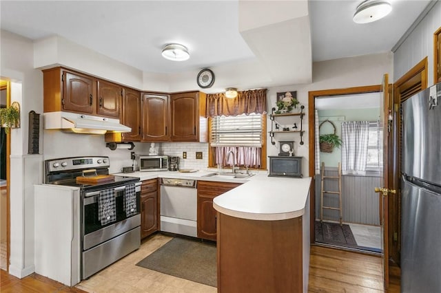 kitchen with under cabinet range hood, a sink, stainless steel appliances, a peninsula, and light countertops