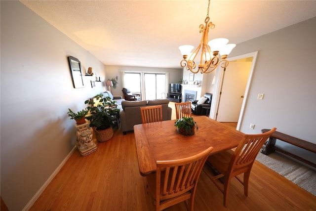 dining area featuring a fireplace, light wood-style floors, baseboards, and a chandelier