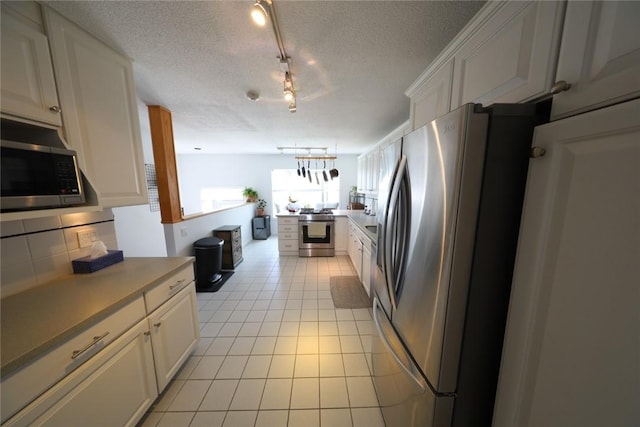 kitchen with a textured ceiling, appliances with stainless steel finishes, white cabinets, light tile patterned floors, and decorative backsplash