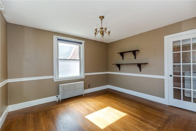 spare room with radiator heating unit, wood finished floors, baseboards, and a chandelier