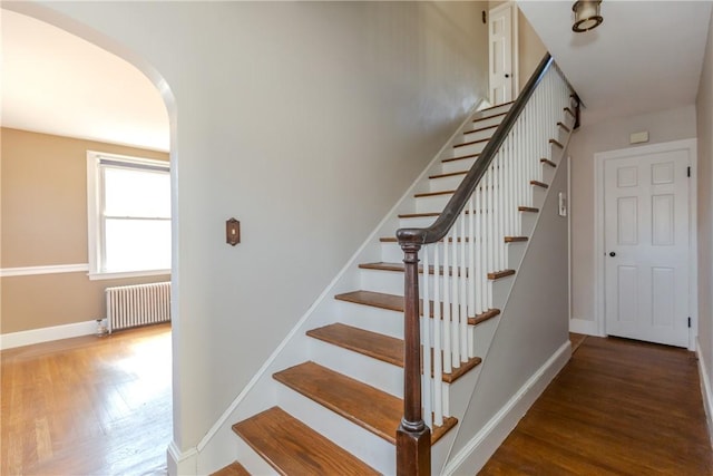 stairway with arched walkways, radiator heating unit, baseboards, and wood finished floors