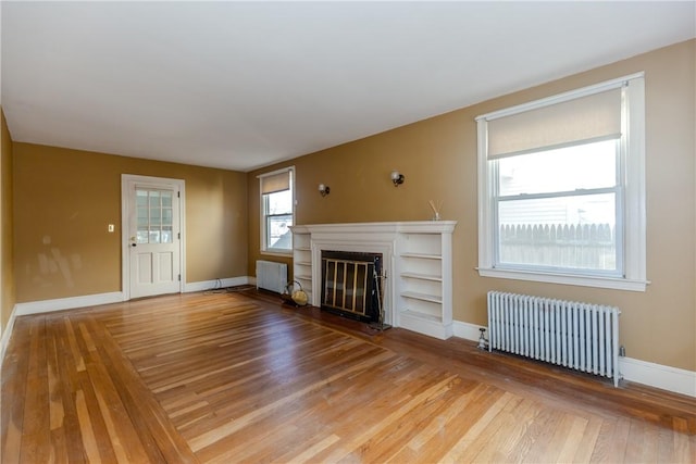 unfurnished living room with a glass covered fireplace, light wood-style flooring, and radiator