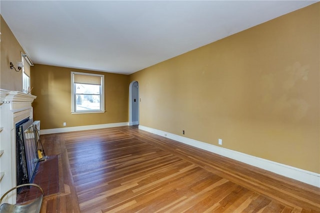 unfurnished living room with wood finished floors, a fireplace, arched walkways, and baseboards