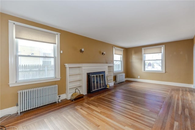 unfurnished living room featuring a glass covered fireplace, radiator, light wood-style floors, and baseboards