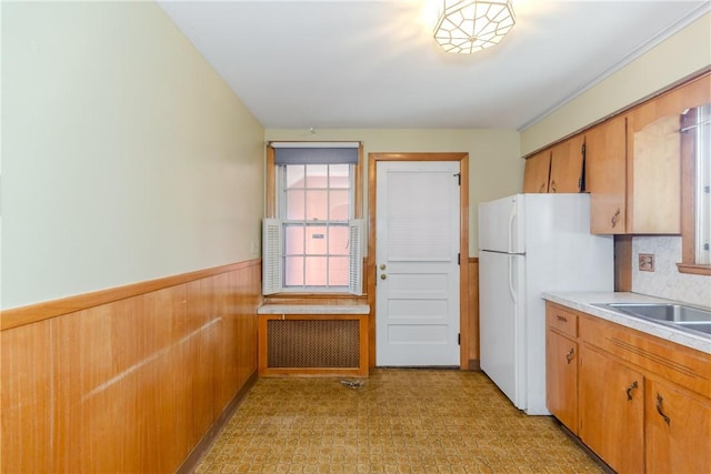 kitchen with wooden walls, a wainscoted wall, light countertops, freestanding refrigerator, and a sink