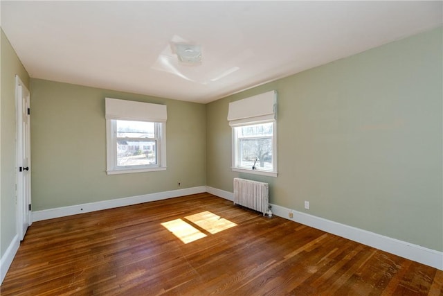 unfurnished room featuring radiator heating unit, baseboards, and wood finished floors