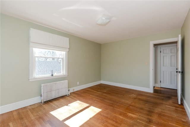 spare room with baseboards, radiator, and wood finished floors