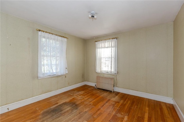 empty room with baseboards, hardwood / wood-style floors, and radiator heating unit