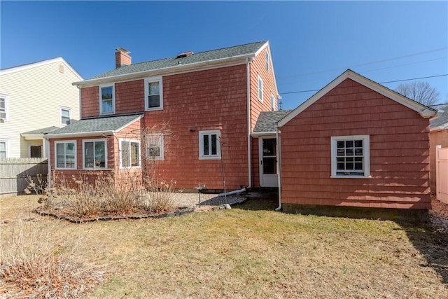 rear view of house with a lawn, roof with shingles, a chimney, and fence