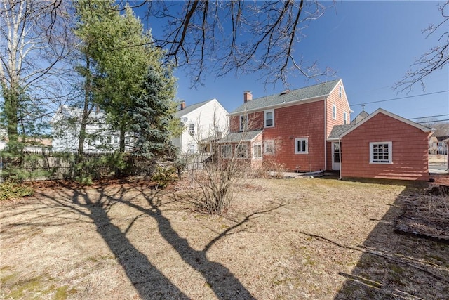 rear view of house with a chimney and fence