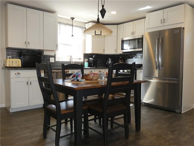 kitchen featuring tasteful backsplash, dark countertops, white cabinetry, stainless steel appliances, and hanging light fixtures