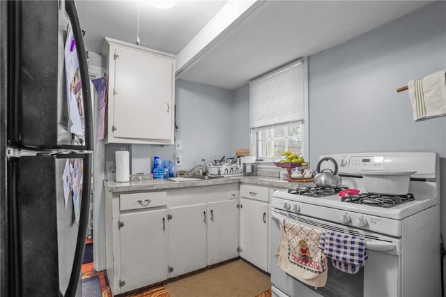 kitchen featuring light countertops, white cabinets, white gas range oven, and freestanding refrigerator