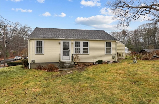 view of front of property featuring entry steps, a front lawn, and a shingled roof