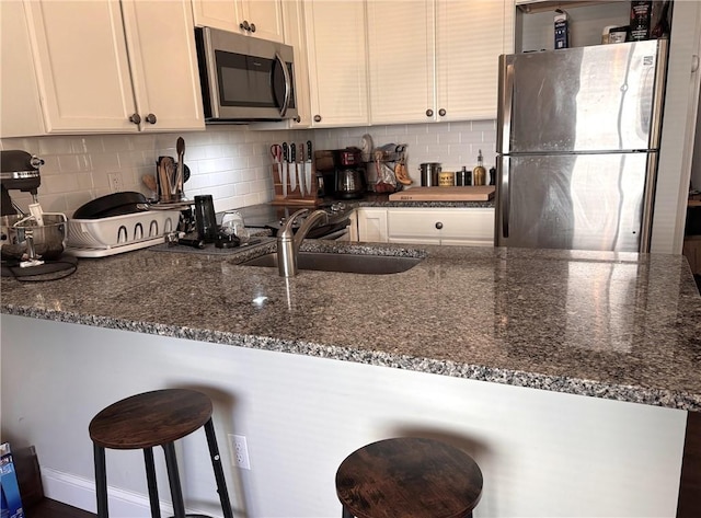 kitchen featuring backsplash, a kitchen bar, white cabinets, stainless steel appliances, and a sink