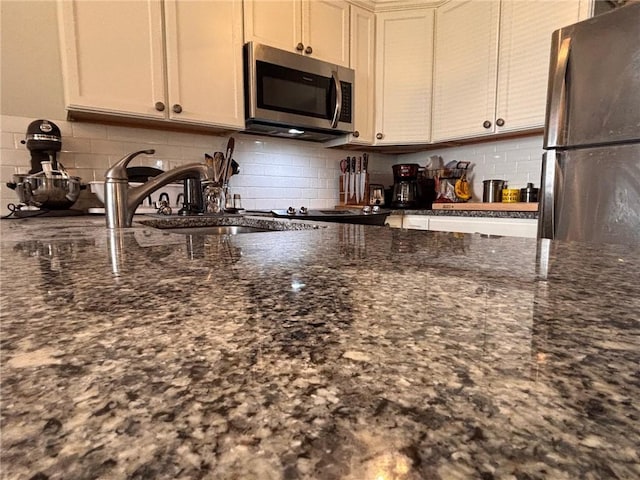 kitchen featuring a sink, dark stone countertops, backsplash, and stainless steel appliances