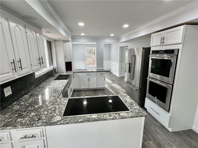 kitchen with a wainscoted wall, a sink, white cabinetry, appliances with stainless steel finishes, and a peninsula