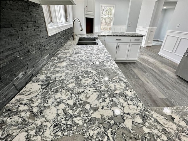 kitchen featuring white cabinetry, light stone counters, wood finished floors, and a sink