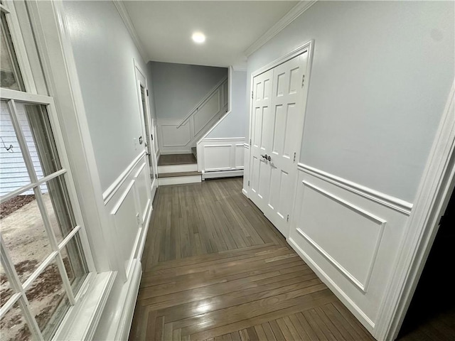 corridor featuring stairway, dark wood-style flooring, ornamental molding, a decorative wall, and baseboard heating