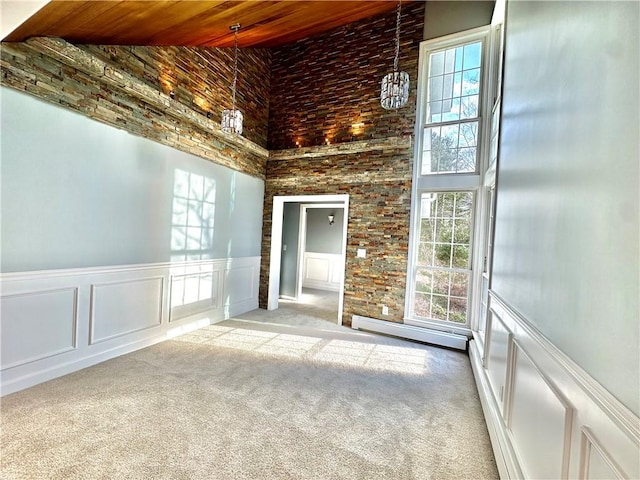 carpeted empty room featuring a decorative wall, a healthy amount of sunlight, wood ceiling, and a baseboard radiator