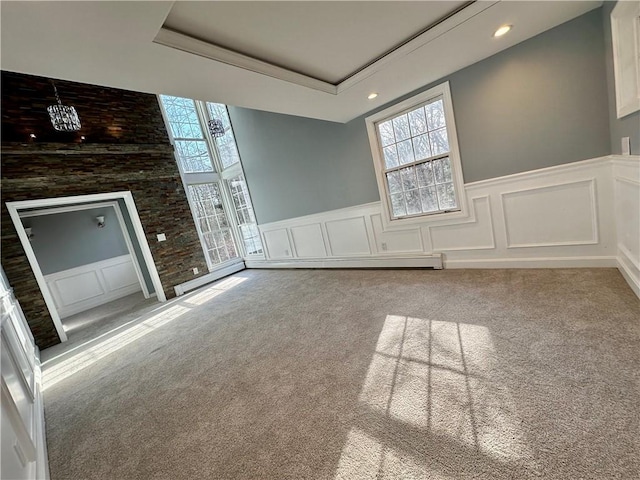 unfurnished living room featuring a tray ceiling, carpet, and wainscoting