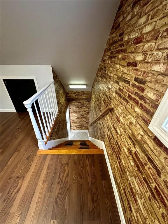 stairs featuring brick wall and wood finished floors