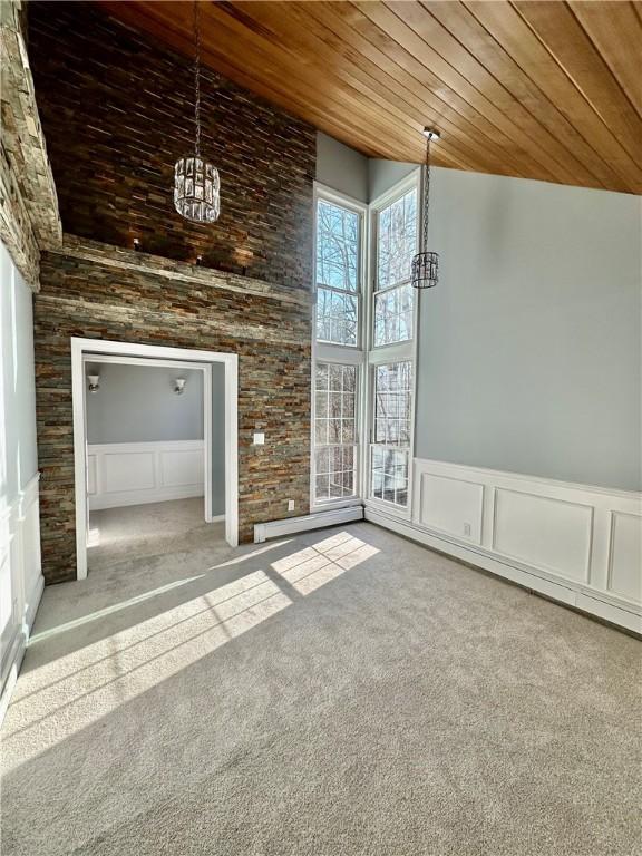 spare room with carpet floors, wainscoting, wooden ceiling, a towering ceiling, and a notable chandelier