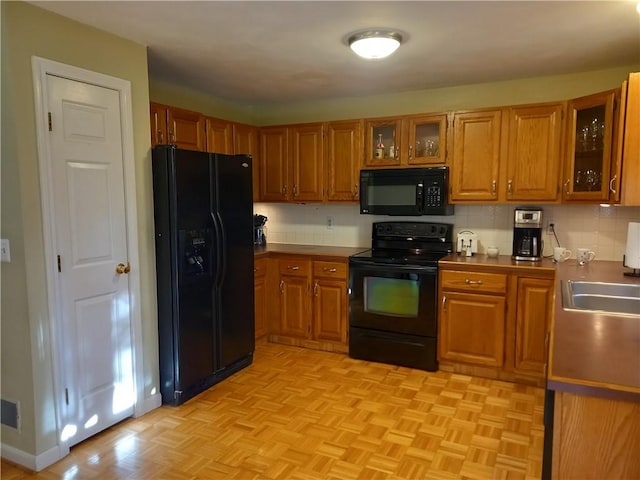 kitchen with brown cabinetry, a sink, decorative backsplash, black appliances, and glass insert cabinets