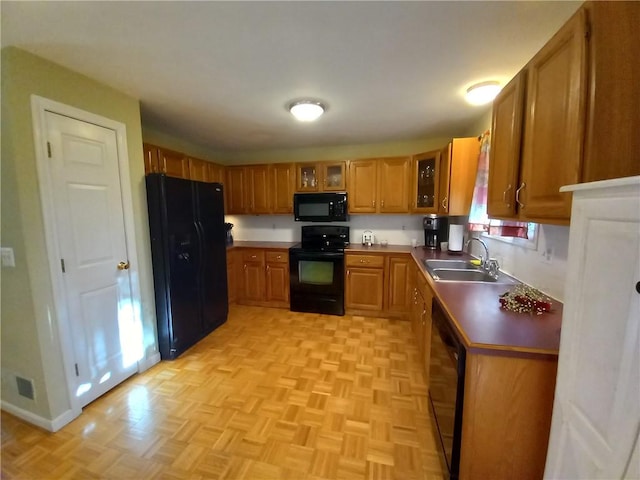 kitchen featuring brown cabinets, black appliances, a sink, glass insert cabinets, and baseboards