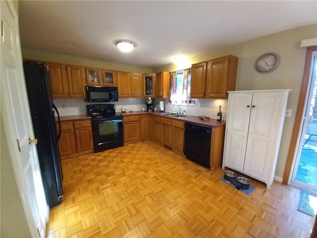 kitchen featuring black appliances, glass insert cabinets, brown cabinets, and a sink