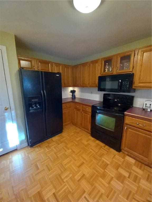 kitchen with black appliances, glass insert cabinets, dark countertops, and brown cabinets